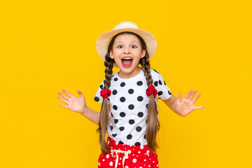 A surprised little girl in a straw hat and summer clothes with polka dots. An astonished child on a yellow isolated background.