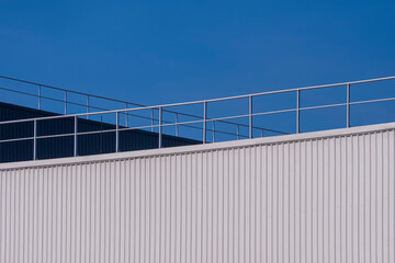 Modern white and black corrugated steel factory buildings wall with aluminium fence on rooftop against blue sky background 