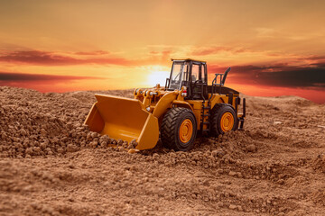 Wheel loader are digging the soil in the construction site on  a sunset background.
