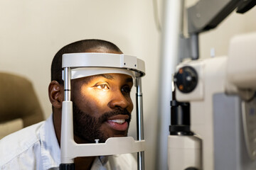 Examination of a dark-skinned man with a slit lamp, microscope, and focused light source. A device for high-precision examination of the eye to determine the condition of the cornea. - obrazy, fototapety, plakaty
