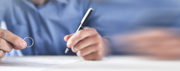 Man holding a wedding ring and signing divorce contract.