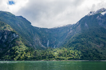a small waterfall tumbles down the cliff side of a fjord in patagonia, aysen region, chile