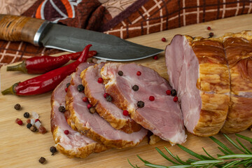 Traditional ham sliced on a wooden cutting board with a carving knife, multi-colored allspice, red hot peppers, parsley, dill and basil. The concept of snacks from pork meat