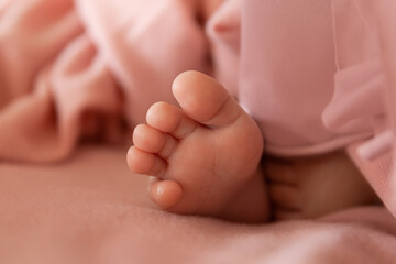 Newborn baby foot on soft wrap as a background in light peach or pink tone, tiny toes of infant
