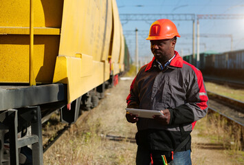 African american railway man with tablet computer at freight train terminal