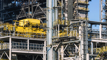 Fototapeta premium Oil refining plant. Technological equipment for the production of fuel components. White smoke escapes into the atmosphere from the production equipment at the refinery. White smoke and blue sky.