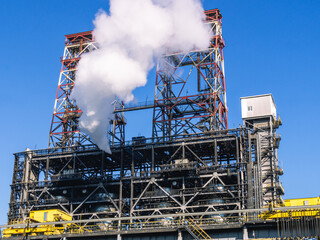 Fototapeta na wymiar Oil refining plant. Technological equipment for the production of fuel components. White smoke escapes into the atmosphere from the production equipment at the refinery. White smoke and blue sky.