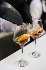 Bartender adding ice cubes from into Aperol spritz cocktail glass. Barman serving orange liqueur cocktail in a wine glass on a bar counter and slice of orange.