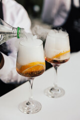 Two glasses of cocktails on the table in the bar. Bartender pours a sprite in glass.
