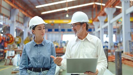 Two professional engineer man and woman manager leader wearing helmet and holding laptop walking in factory talking and discussing for work