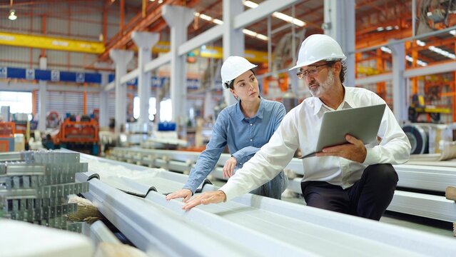 Two engineer manager leader and woman assistant discussing and explaining detail holding laptop talking and checking production of metal sheet roof at metal factory. Recruitment concept - Powered by Adobe