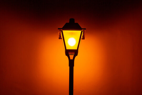 Um poste com uma luminária vintage de iluminação pública, acesa, durante a noite.