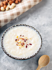 Indian rice kheer with nuts on a gray background. Bowl with rice pudding and a linen napkin on concrete. Top view
