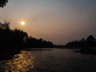 Vintage sunset with silhouette of trees along with river bank.