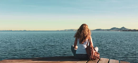 Foto op Plexiglas Beautiful woman sitting on wooden pier and looking at the sea- freedom, peaceful,  travel concept © M.studio