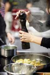 girl cook spices potatoes, wooden pepper pot. the cook sprinkling potatoes with spices from a...