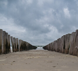 Eine Doppelreihe Holzpolder führt den Blick zur Nordsee unter einem düsteren Wolkenhimmel