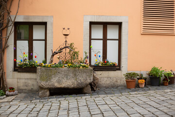 Fototapeta na wymiar Rustikale Schönheit: Blumengeschmückte Fenster und antiker Steintrog in Rothenburg o. d. Tauber