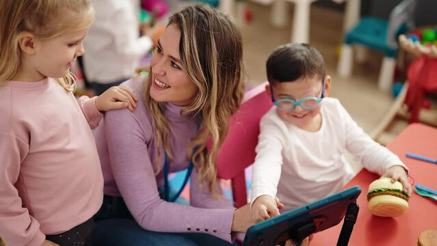 Woman with boy and girl having lesson using touchpad at kindergarten