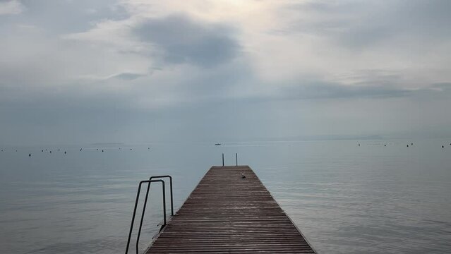 The wooden pier on the Italian Garda lake with tranquil water with no waves 