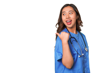A young nurse chinese woman points with thumb finger away, laughing and carefree.