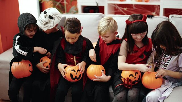 Group of kids wearing halloween costume putting candies in pumpkin basket at home
