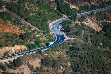 Truck with refrigerated trailer driving on a winding mountain road, aerial view.