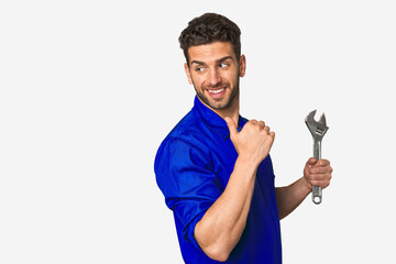 Young mechanic man holding a wrench points with thumb finger away, laughing and carefree.