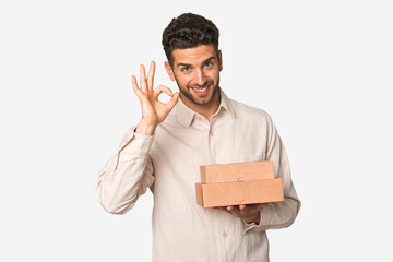 Young man holding a takeaway boxes isolated cheerful and confident showing ok gesture.