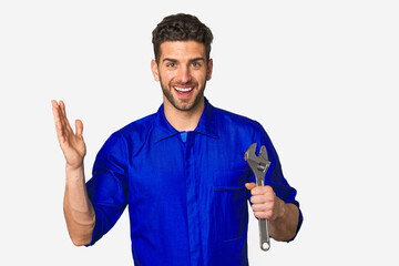 Young mechanic man holding a wrench receiving a pleasant surprise, excited and raising hands.