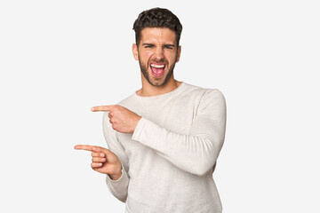 Young handsome man isolated pointing with forefingers to a copy space, expressing excitement and desire.