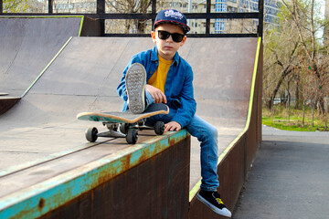 a boy in a cap and glasses is sitting on a ramp with a skate
