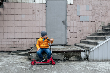 A little boy with a scooter next to an abandoned building