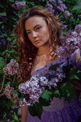 Spring style. A young woman in a beautiful dress in a garden with blooming purple bushes. Blooming spring garden.