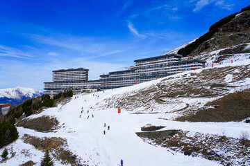 Large residential building surrounded by ski slopes on a mountainside in Les Ménuires ski resort in the French Alps - Skiers following a track circling a hotel in winter