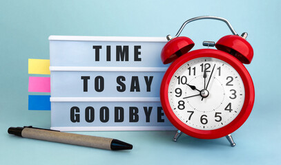 Text TIME TO SAY GOODBYE? written on the lightbox with alarm clock and colorfull stickers on blue...