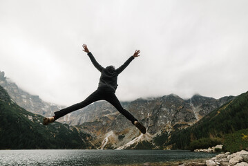 A Man jumping on the stony shore near the lake in the mountains. Boy against the backdrop of a mountain landscape. Scenic mountain view.
