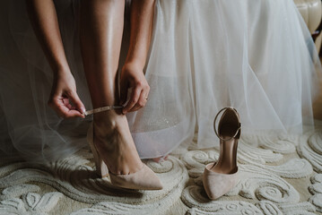 Bride putting her stylish classic beige shoes. Wedding morning preparation in home. Close up.