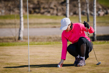 A woman is marking a golf ball on the green in the spring