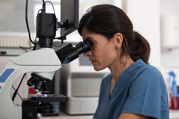 side view of female veterinarian looking through the microscope of the microscope.