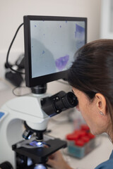 closeup of female veterinarian looking through microscope with digital display.