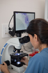 female veterinarian looking through microscope with digital display.