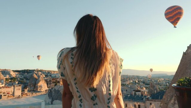 Happy beautiful woman runs towards incredible view of hot air ballons in Cappadocia and looks back at camera.