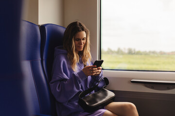 Modern people city lifestyle. Young urban blonde woman using phone app, chatting, scrolling social media pages. Girl enjoying train travel in business class seat. Transport travel lifestyle.
