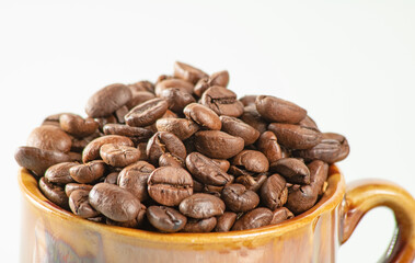 Coffee theme. Ceramic cup filled to the brim with coffee beans on a white background