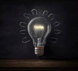 Light bulb on black blackboard with wooden tabletop in front, Generative AI