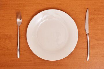 Empty and clean white plate with fork and knife on a wooden table as an example of table etiquette