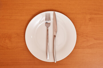 A signal "The dish is wonderful". Empty and clean white plate with fork and knife on a wooden table as an example of table etiquette