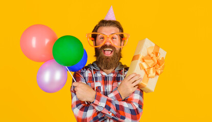 Happy bearded man in funny glasses and birthday hat with present box and balloons. Handsome guy...