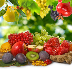 various fruits: figs, kiwi, cranberries, ginger, pomegranate, grapes, lemon and sea buckthorn which lie on white and grapes, grapefruit and pomegranate hanging from above on a green blurred background